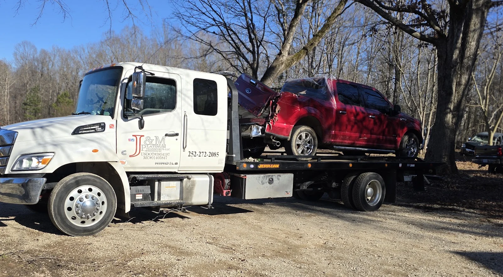The J&M Platinum Transports flatbed rollback with a wrecked pickup loaded and strapped down on the deck